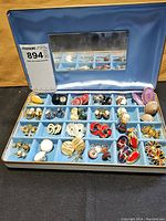 Blue velvet-lined jewelry case open showing 30 pairs of assorted earrings arranged in compartments with a mirror inside the lid.