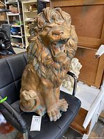 Front view of a large plaster lion statue with detailed mane and open mouth, sitting on a black chair.