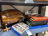 Photo showing several vintage photo albums in various colors stacked on a shelf beside a wooden barrel-style storage box and an open album with old photos visible.
