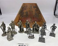 Photo showing all 10 pewter president figures arranged in a row with a vintage lamp shade in the background featuring a historic building.