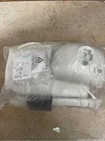 Top view of the white portable camping sink wrapped in clear plastic showing hose and fittings.