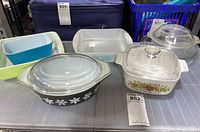 Overview photo showing multiple vintage glass bakeware pieces on a table including Pyrex and Glasbake casseroles and bake dishes with lids.