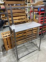 Full view of the rolling metal shelf, showing the three shelves with wire and solid surfaces and caster wheels at the bottom.