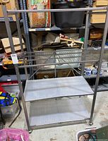 Front view of the rolling metal shelf showing three wire grid shelves and one solid lower shelf on wheels