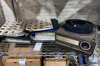 Sears Continental 55 projector with 3 binders of film slides stored on a metal shelf. The slides appear to be mounted film slides with subjects such as zoo animals and travel destinations.