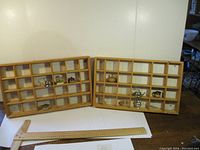 Two wooden display shelves on floor with small ornaments inside compartments, accompanied by ruler for scale.