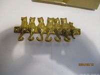 Brass key holder with seven cat figurines in a row, tails as hooks, placed on white background.