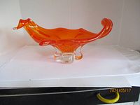 Orange chalet style art glass bowl on a white background, showing side view with curled ends on rim and clear glass base feet.