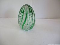 Side view of green and clear glass egg showing swirled ribbons and intricate cut patterns