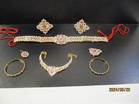 Full set of eight-piece costume jewelry with pink stones laid out on black background