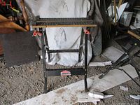 Image showing the fold up Jobmate workbench with wooden slatted top and orange clamps in a dusty workshop environment.