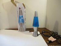 Photo of the 11.5 inch tall blue liquid lava lamp with silver base and cap, alongside its original box and power cord.