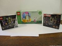 Three LEGO sets on a white background: Spring Garden House in center, Marvel sets on each side