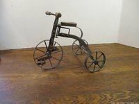 Side view of metal display bike showing large front wheel with pedals and two smaller rear wheels with seat and handlebars with wooden grips.