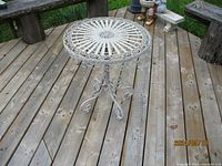 White decorative metal patio table featured outdoors on wooden deck, showing top and base details