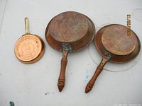 Three copper frying pans seen from underside showing wooden handles and patina.