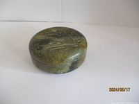 Round soap stone trinket box sitting on white surface, showing the side profile and lid fit.