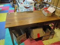 Full view of the solid oak table showing rectangular top surface and thickness, placed in environment with colorful foam floor mats and surrounded by boxes.