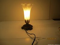 Lit tulip-shaped frosted glass lamp showing the warm light and ornate metal base.