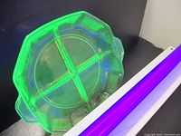 Top-down view showing the vibrant green glow and five divided sections of the uranium depression glass bowl under UV light.