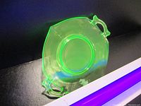 Top view under UV light showing bright fluorescent green uranium glass plate with two handles.