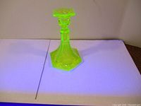 Uranium vaseline glass candle holder glowing under UV light, showing bright neon green color.
