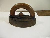 Side view of vintage sad iron showing wooden handle attached to cast iron base with knob on top.