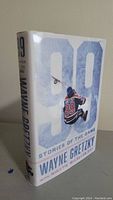 Front and side view of hardcover book '99 Stories of the Game' by Wayne Gretzky showing dust jacket with hockey themed imagery and large '99' graphic.