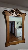 Full view of the antique wooden wall mirror showing the carved decorative top and smooth wooden frame around rectangular mirror glass.