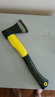 Front view of hand axe showing blade covered with black protective head and yellow and black handle with textured grip dots