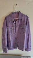 Front view of brand new men's purple denim jacket hanging on hanger, showing button-up front and chest pockets.