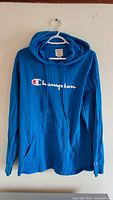 Front view of a blue Champion hoodie hanging on a white hanger, showing the logo on chest