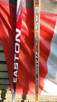 Pair of Easton hockey sticks propped against a Canadian flag; one is red and white, the other is natural wood color with Classic branding.