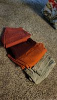 Four folded pairs of men's pants in various colors photographed on carpet.