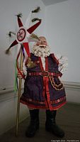 Santa figurine dressed in purple and red with a star-shaped ornament in hand, displayed against a plain wall.