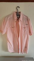 Front view of the light pink short sleeve button-up Columbia shirt hanging on hanger