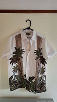 Front view of white button-up shirt with brown and green palm tree design on front sides and bottom hem.