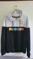 Front view of the sweater showing the black and gray color block, colorful PLAYBOY logo with flower, and kangaroo pocket.