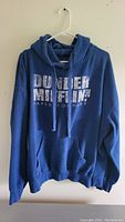 Blue hoodie sweater with Dunder Mifflin Paper Company logo on front, hanging on white hanger