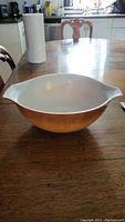 Side view of vintage Pyrex Cinderella mixing bowl showing brown/orange exterior and white interior on wooden table
