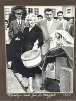 Close-up of the black and white 1954 photograph showing Marilyn Monroe and Joe DiMaggio walking, Marilyn holding a hatbox, signed/captioned in white text.