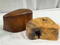 Two hand-shaped carved wood boxes, one in burl wood with natural hollow and felt lining, the other in darker wood with fabric lining.
