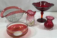 Full view of all five cranberry and red glass items including two bowls and three vases/dish with decorative trim and applied motifs.