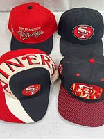 Four San Francisco 49ers caps arranged in two rows on white background.