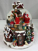 Full view of Christmas snow globe showing Santa Claus, elves, Christmas presents, and snow-covered village base.