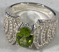 Front view of sterling silver ring showing round green peridot and decorative silver detailing with additional small clear stones.