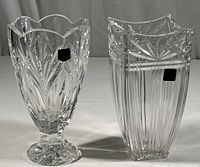 Two crystal vases side by side, showing the overall shape and size difference, with one having a pedestal base and scalloped rim and the other a square shape with vertical cuts