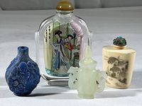Four Chinese snuff bottles and decorative glass bottle displayed together on white surface.