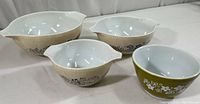 Set of three beige handled Pyrex bowls with blue floral Homestead pattern and one green Crazy Daisy 1.5-pt bowl on white background