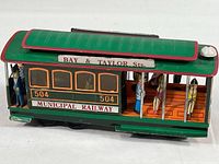 Front side view of the tin cable car toy showing Bay & Taylor Sts. sign, Municipal Railway text, and figures visible inside.